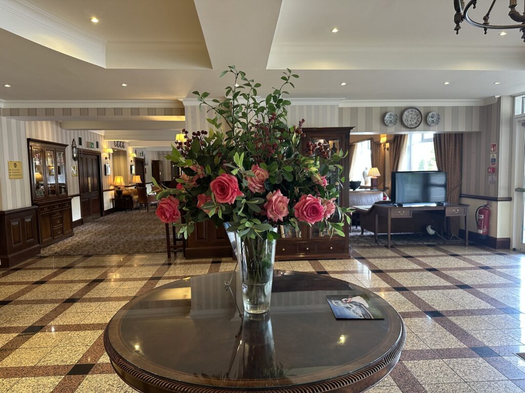 Pink garden roses, berries and foliage in a tall glass vase on a round table in a hotel lobby